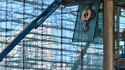 Man on a cherry picker guides a large sheet of glass held by a crane in to place.
